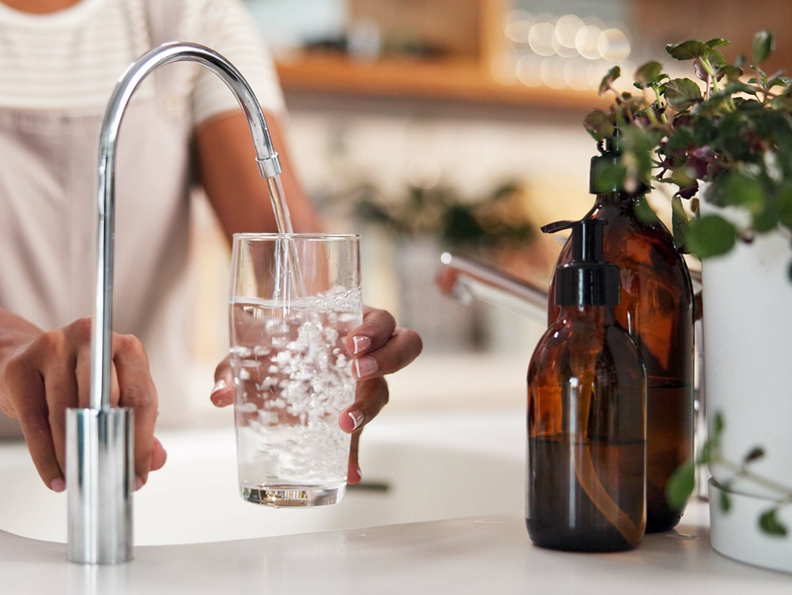 Hand filling a glass with sparkling filtered water from a kitchen faucet